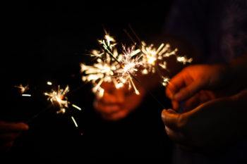 Cropped Image Of People Holding Sparklers Against Black Background
