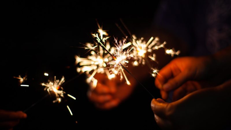Cropped Image Of People Holding Sparklers Against Black Background