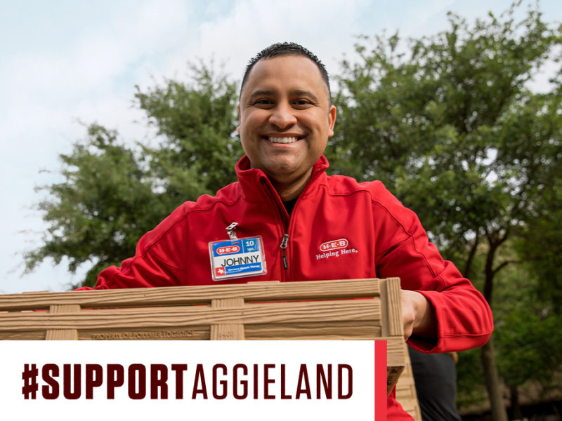 heb employee wearing red jacket and nametag holding crate with support aggieland graphic overlay