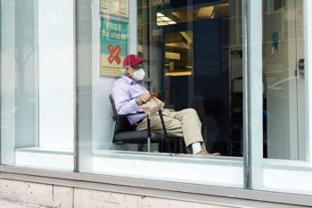 A man wearing a protective mask sits next to a sign offering free flu shots