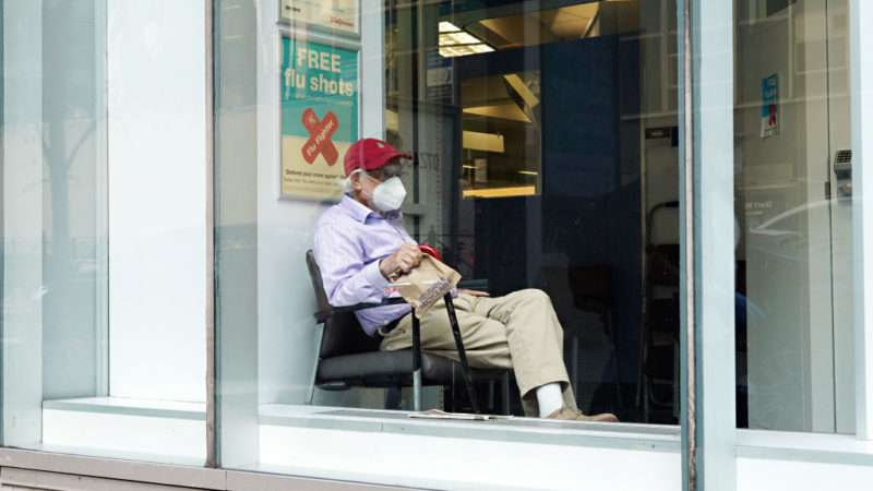 A man wearing a protective mask sits next to a sign offering free flu shots
