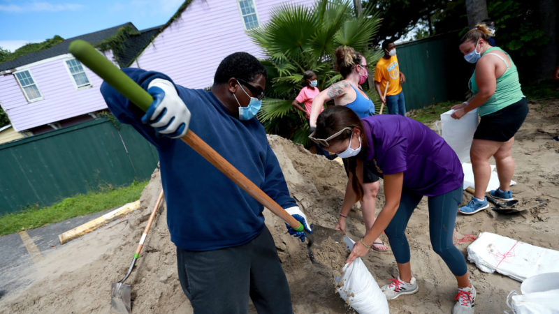 people wearing medical face masks shovel sand into sandbags