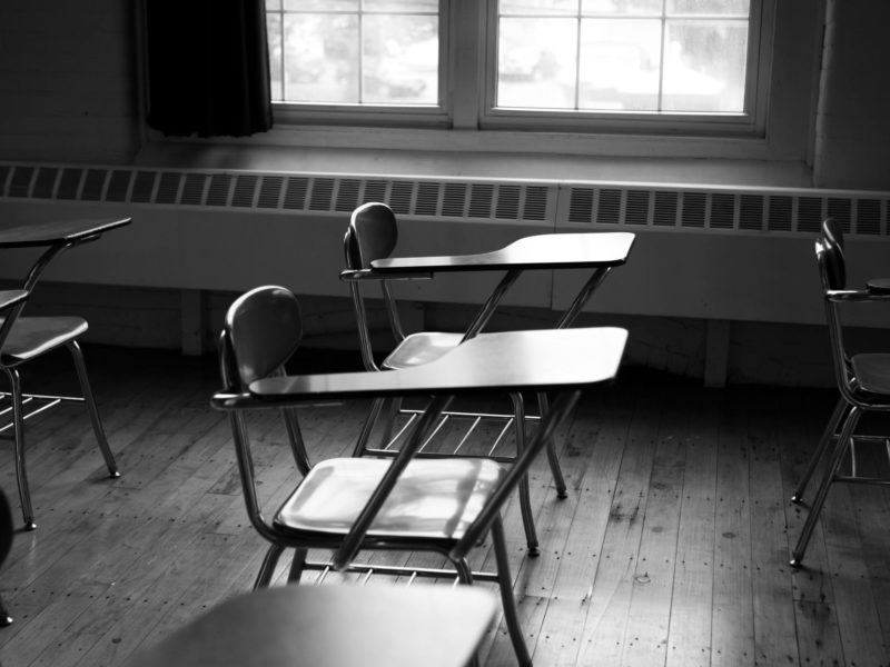 black and white photo of empty desks in a classroom