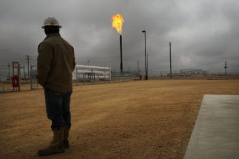 worker standing in field looks at a natural gas flare against a dark sky