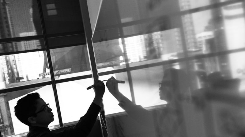 a black and white photo of a man drawing on a whiteboard