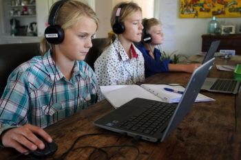 a photo of three children doing homeschool on laptops