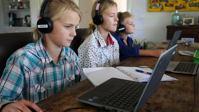 a photo of three children doing homeschool on laptops