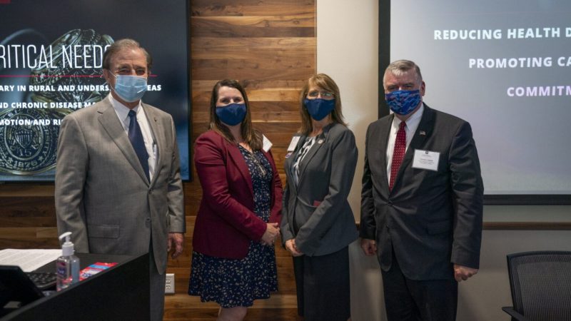 2 men and 2 women all wearing covid masks and professional attire are looking towards the camera and are all smiling