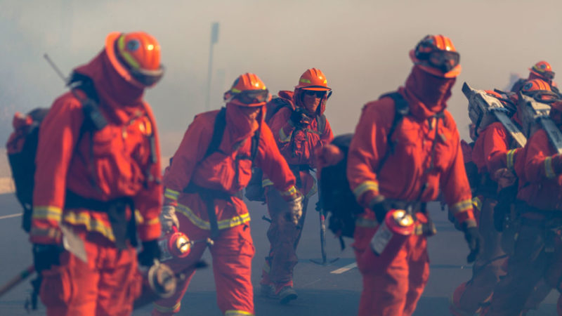 inmates wearing bright orange fire fighting uniforms walk through smoke