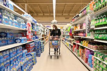 woman wearing face mask pushing shopping cart down grocery store aisle