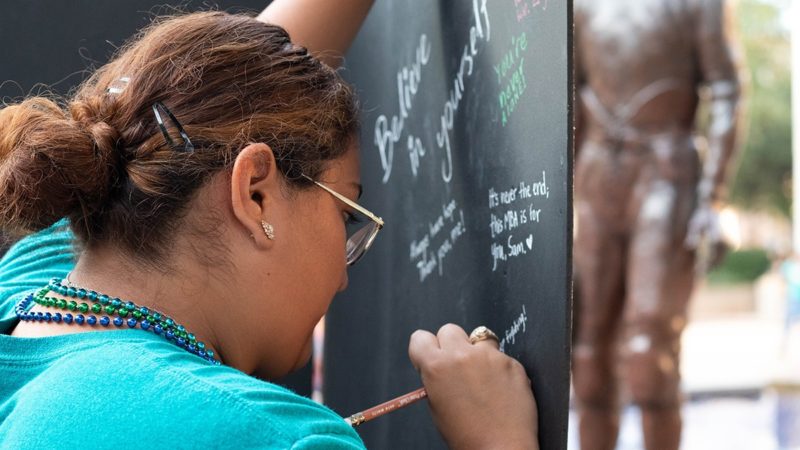a Texas A&M student writes on a large chalkboard outside on campus