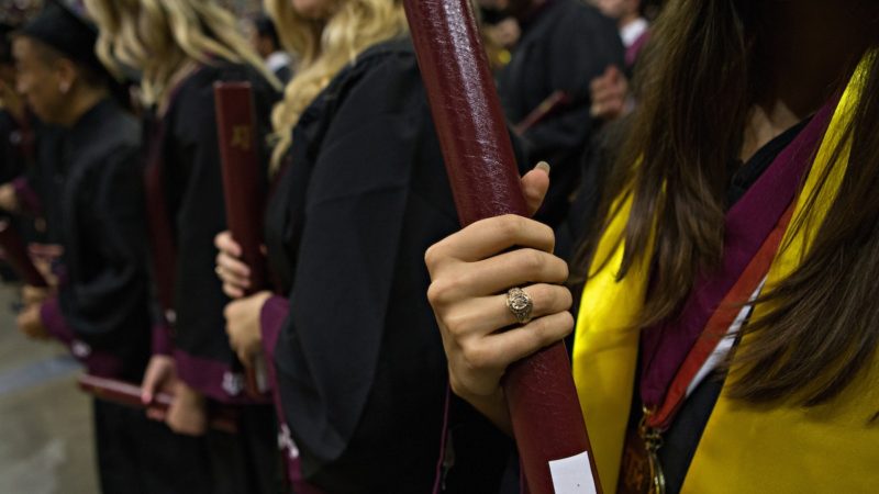 close up of woman in cap and gown standing in row of graduates holding diplomas