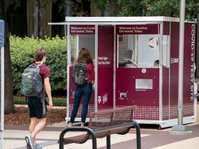 two students walk up to maroon kiosk for testing