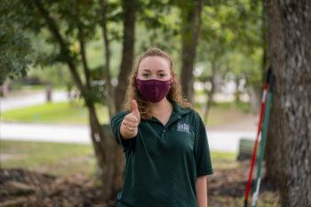 a photo of a student wearing a mask and a Big Event shirt giving the gig em thumbs up