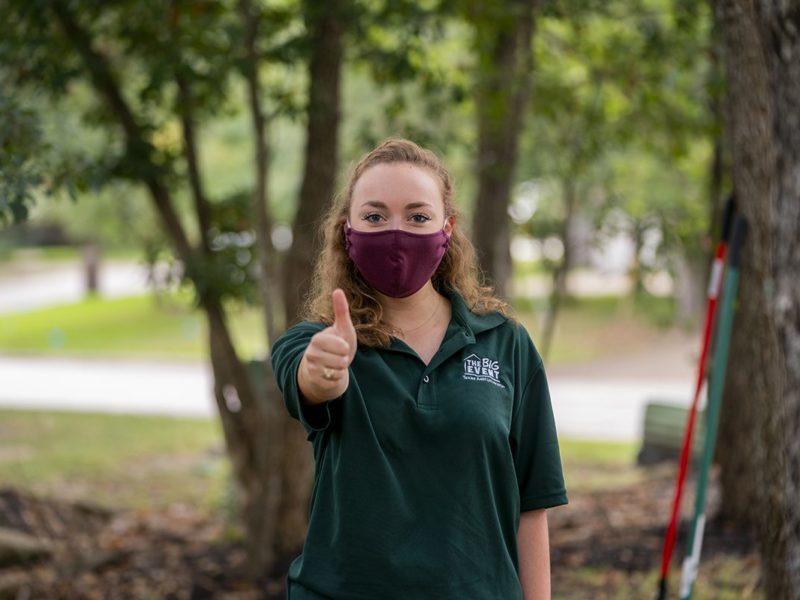 a photo of a student wearing a mask and a Big Event shirt giving the gig em thumbs up