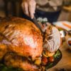 Close up of person carving turkey at dining table.