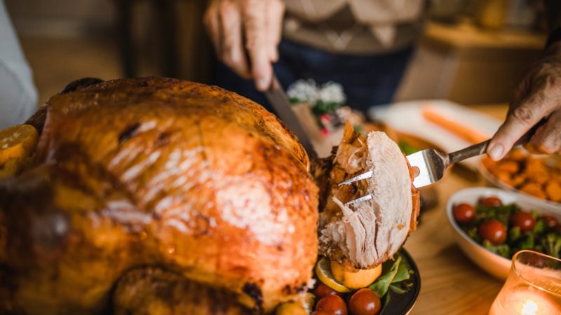 Close up of person carving turkey at dining table.