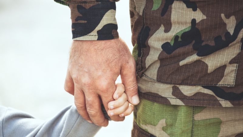 close up of man wearing army fatigues holding small child's hand