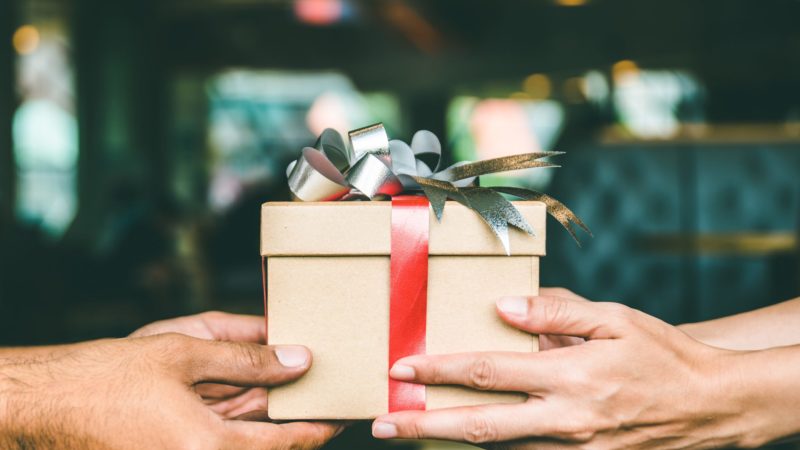 Cropped Hand Of Man Giving Christmas Present To Female Friend
