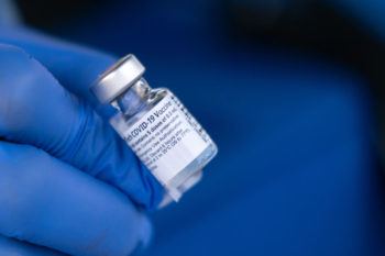 close up of gloved hand holding a vial of the vaccine