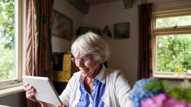 an elderly woman uses a tablet in her kitchen