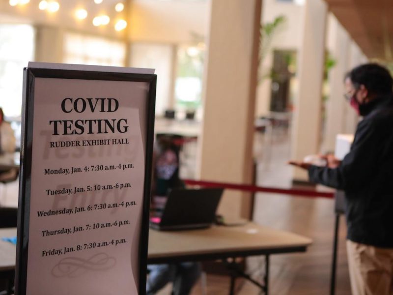covid testing sign in front of table where man talks to seated volunteer