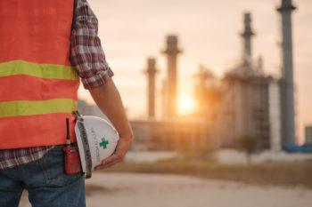view of engineering from behind wearing safety vest and holding helmet in front of a power plant