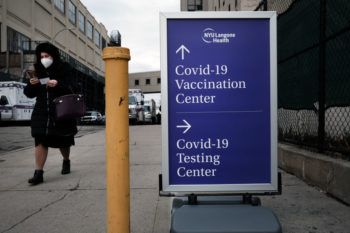 Person walks by a purple sign advertising covid-19 vaccinations and testing