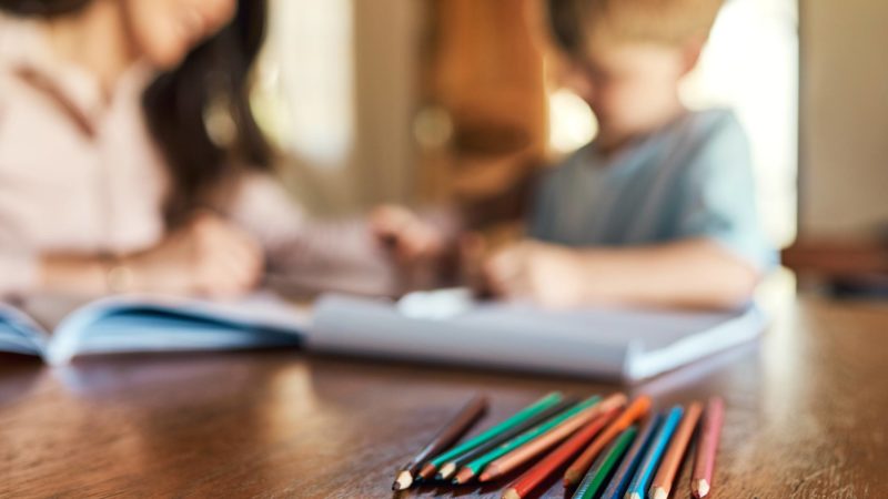 Shot of pencils on a table with a mother and son doing homework in the background