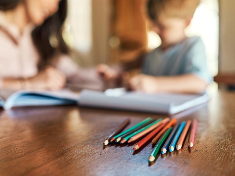 Shot of pencils on a table with a mother and son doing homework in the background
