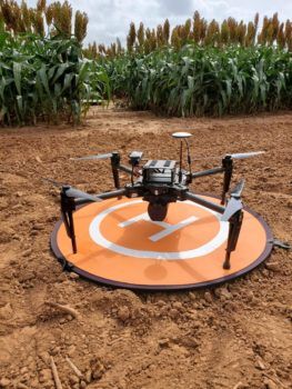 a drone sitting on the ground in front of a field of corn