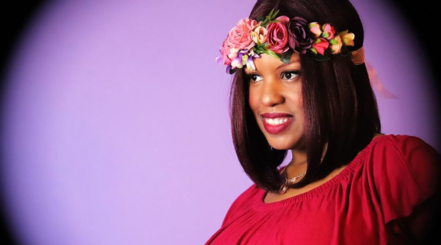 an indoor portrait of a woman wearing red with flowers in her hair in front of a purple background