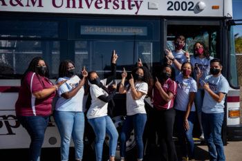 Members of the Matthew Gaines Society pictured with a Texas A&M bus displaying the route named in Gaines' honor.
