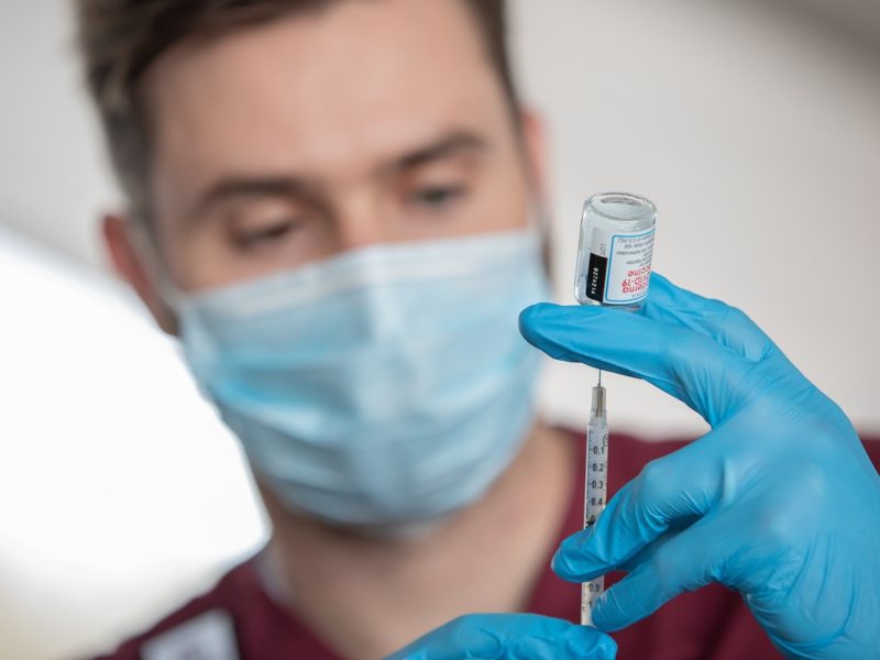 nursing student putting a syringe in a vial of the covid vaccine