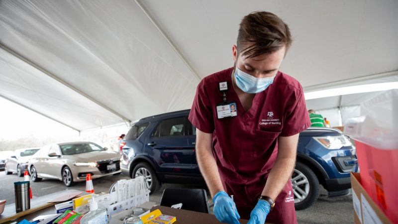 male student in maroon scrubs prepares a dose of the vaccine
