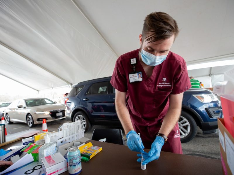 male student in maroon scrubs prepares a dose of the vaccine