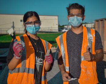 students in orange construction vests and face coverings give the gig 'em