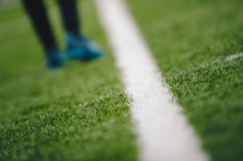 Sports grass field and white sideline. Sports player walking in the blurred background