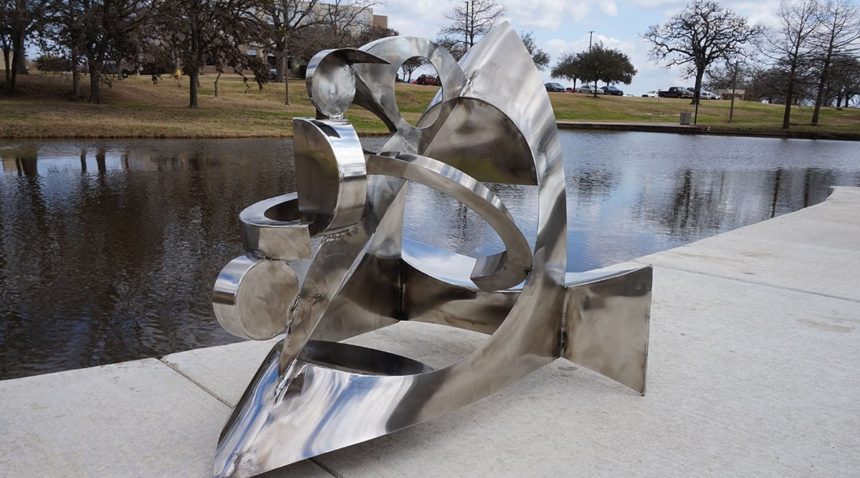 a steel sculpture displayed in front of a pond