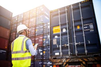 man standing in foreground in front of stacked shipping containers