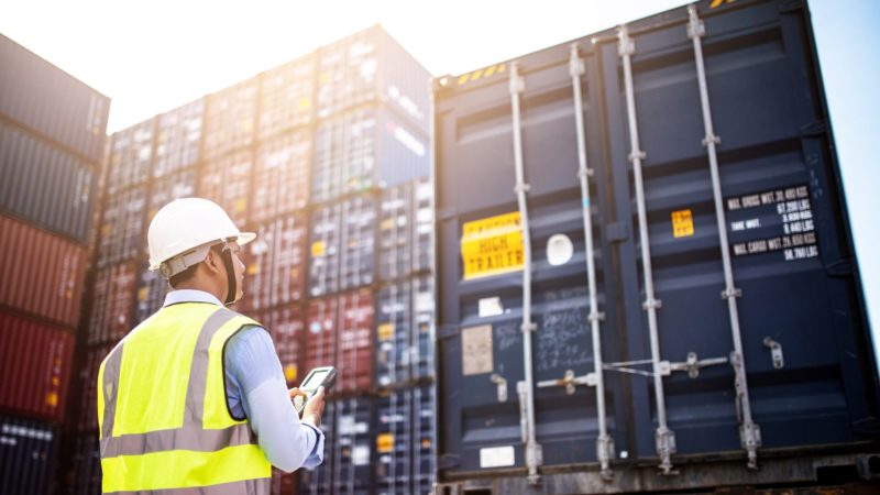 man standing in foreground in front of stacked shipping containers