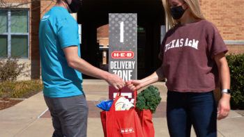 a photo of an HEB employee handing a delivery order to a customer