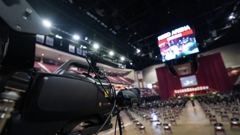a large camera points toward the empty floor of reed arena before a commencement ceremony