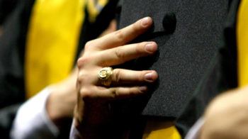 a photo of a man's hand wearing an Aggie ring and holding a graduation cap to his chest