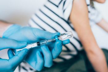 Hands with protective gloves fills syringe with vaccine.