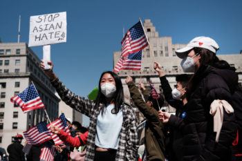 a group of people protest outside, holding american flags and signs tht say "stop asian hate"