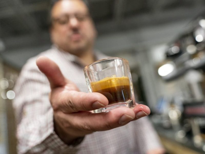 close up view of man holding a shot of espresso in his hand