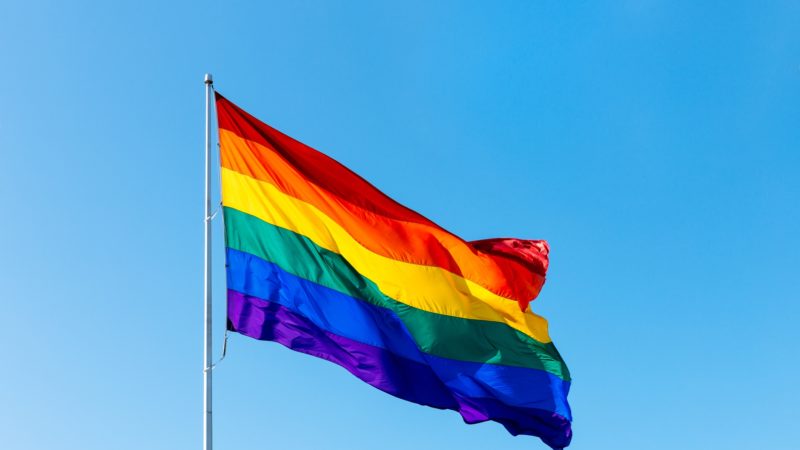 rainbow lgbtq flag waving against a blue sky