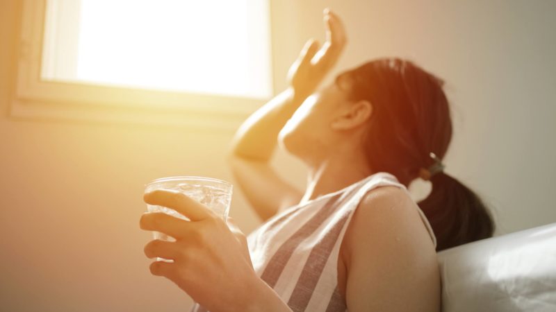 woman holding a glass of water looks into the sun through a window