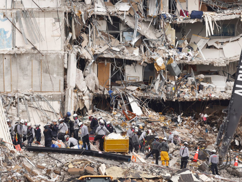 search and rescue crew standing on rubble pile in front of collapsed building